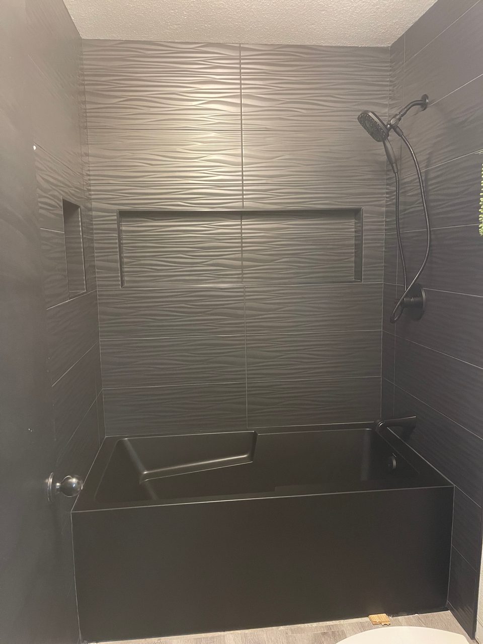 Finished tub and shower surround in grey textured wave tile with a black tub and handheld shower fixture