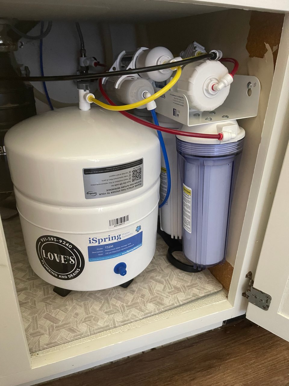 Under-sink iSpring reverse osmosis drinking water system with storage tank and filter housings, labeled with a Love’s Plumbing and Drains sticker