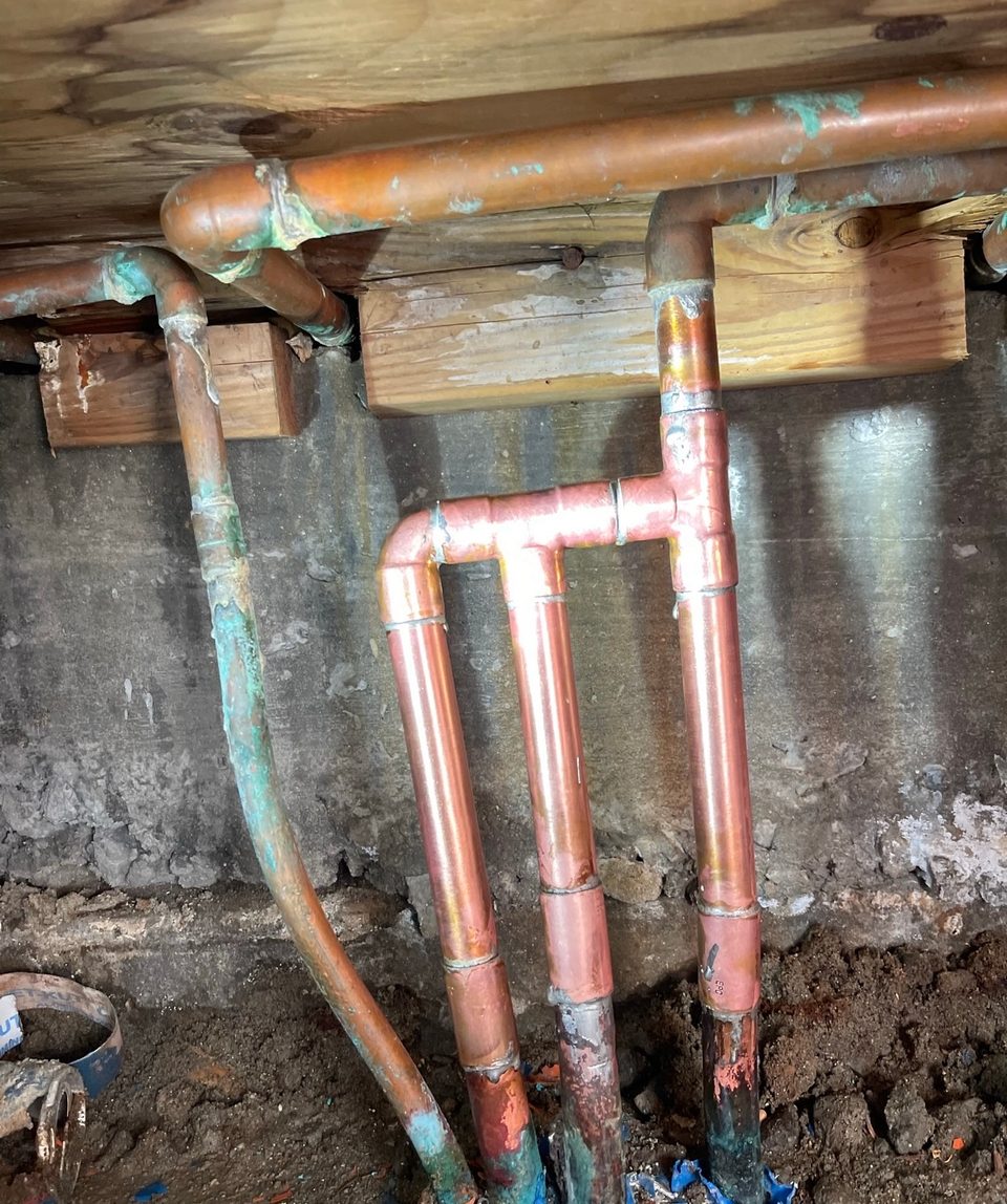 New copper supply manifold installed against a concrete foundation wall in a crawlspace
