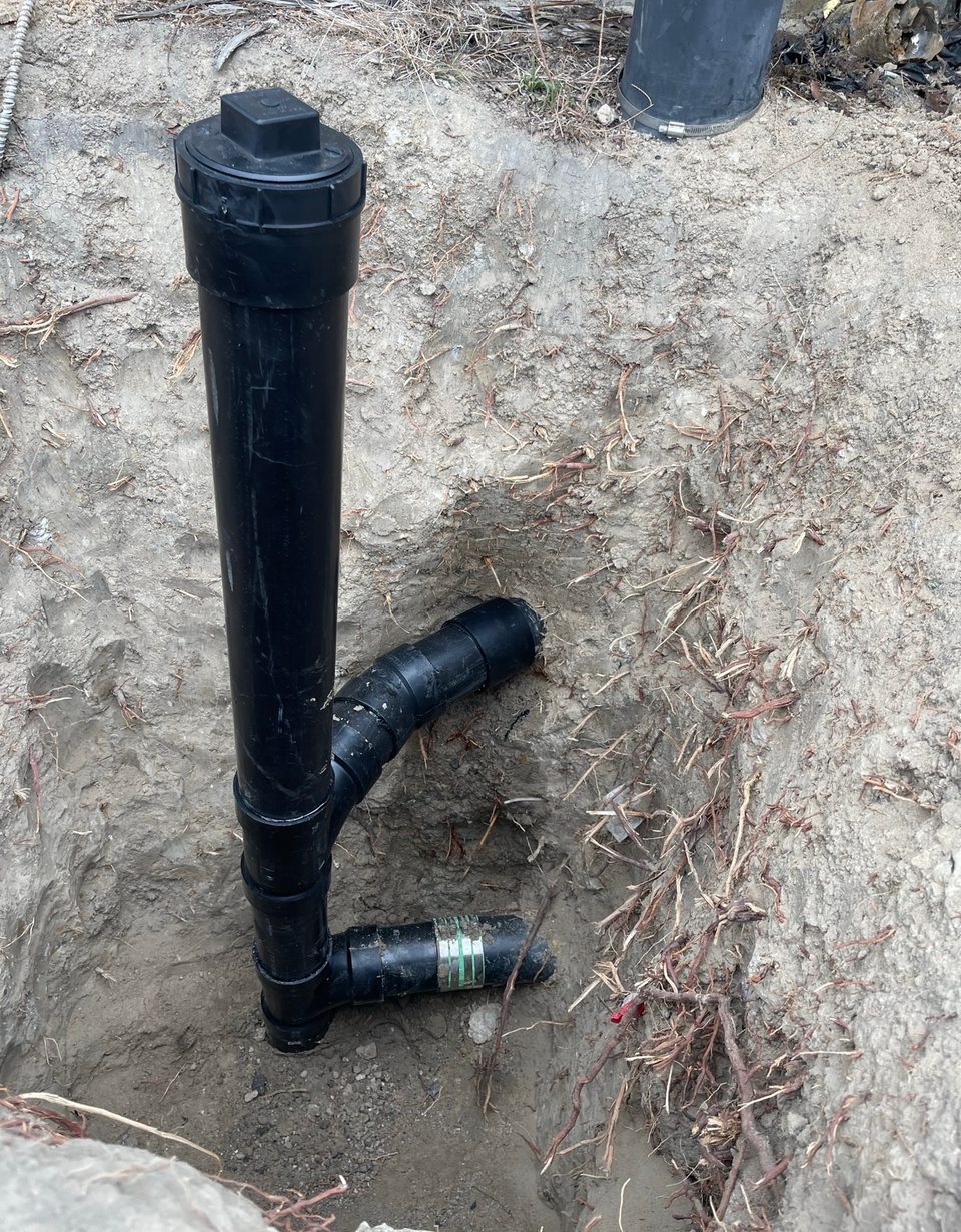 Capped black ABS sewer cleanout riser installed on a new drain line in an excavated trench