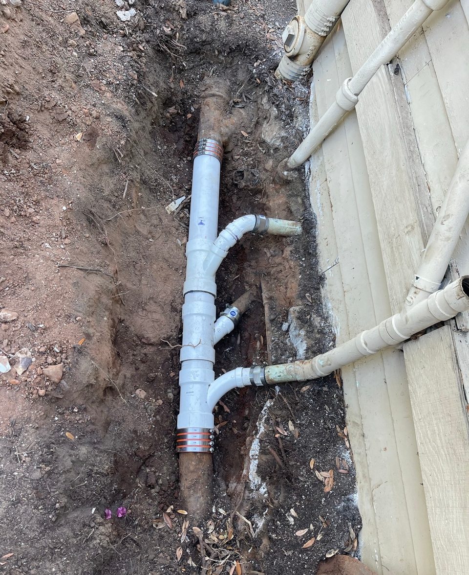 Existing sewer line uncovered in a shallow trench alongside a building during a drain repair