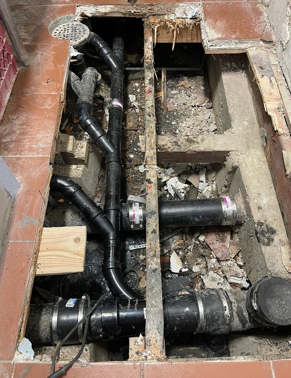 Under-slab drain replacement with new black ABS pipe and fittings run through an opened tile floor