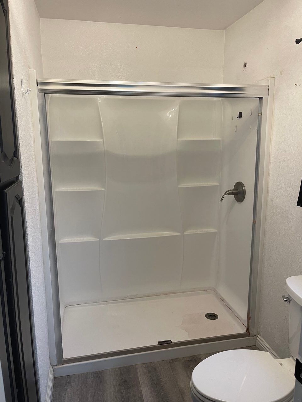 Newly installed white shower enclosure with sliding glass doors and a brushed nickel valve