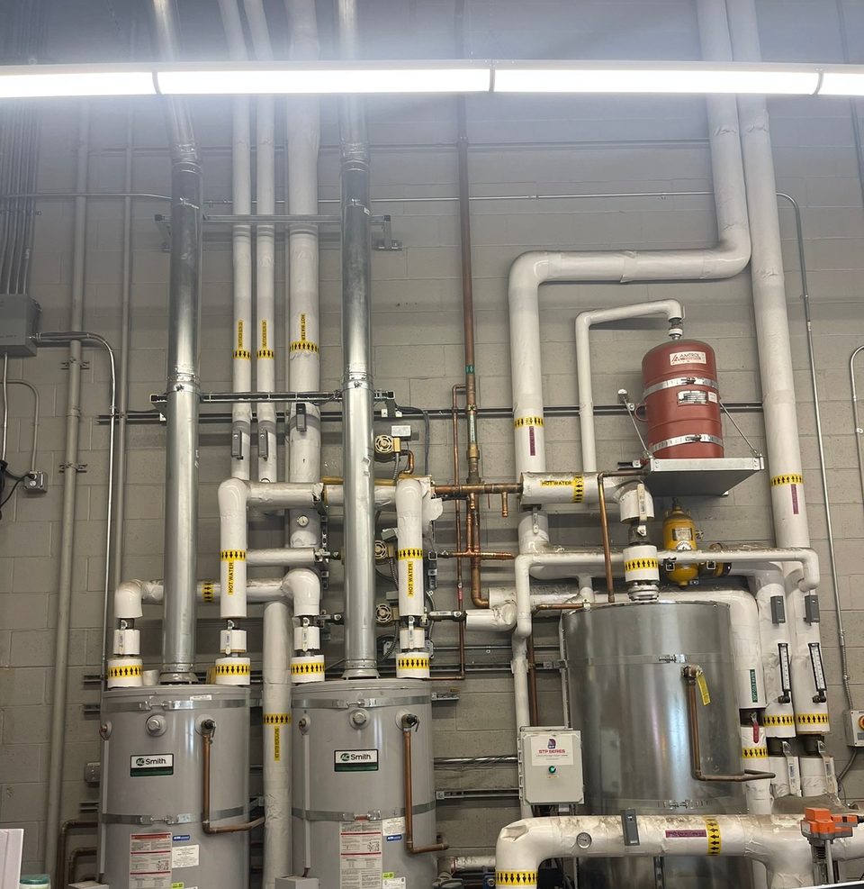 Bank of commercial water heaters with insulated supply piping, expansion tank and stainless storage tank in a mechanical room