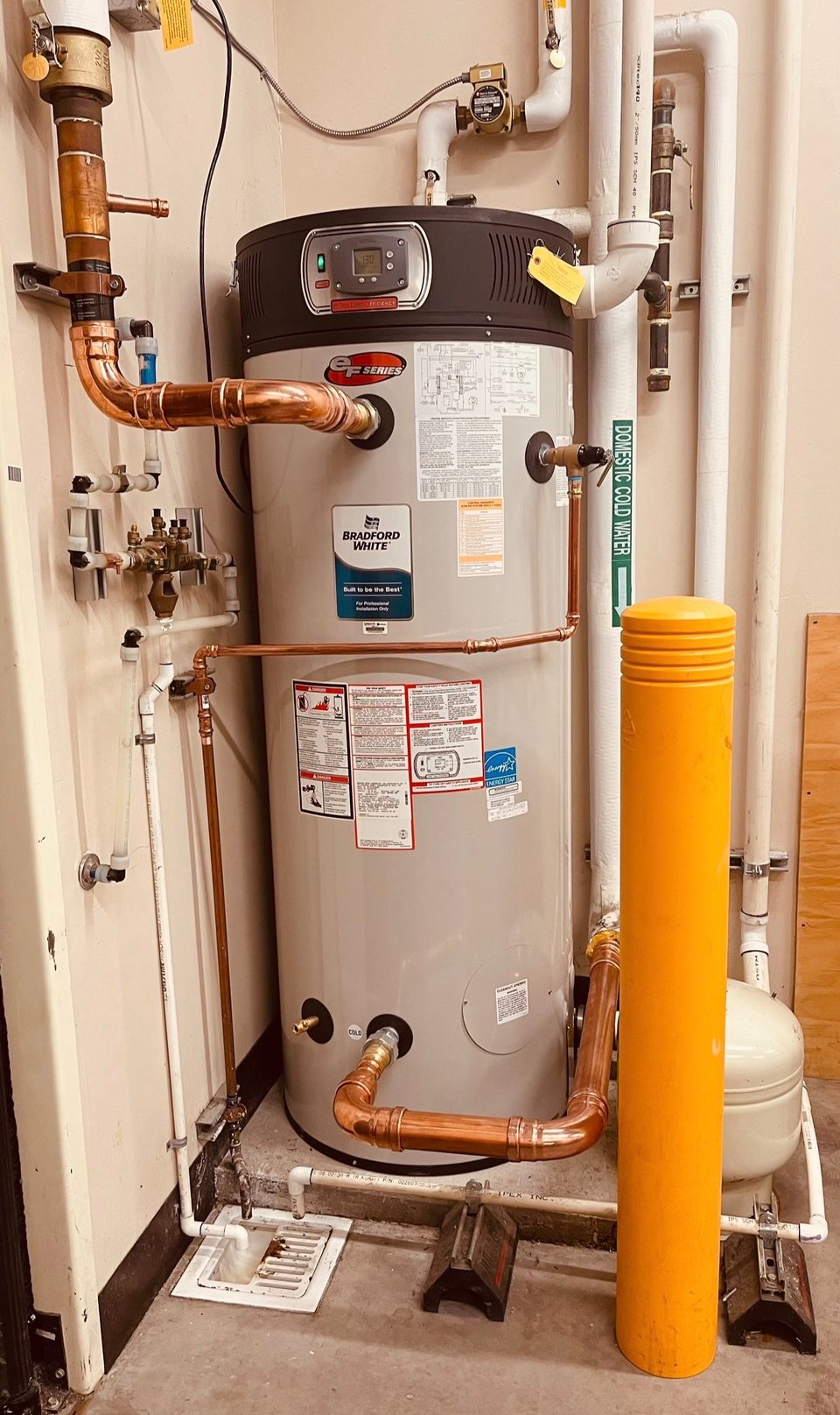 High-efficiency Bradford White commercial water heater with copper supply lines and a gas shutoff in a mechanical room